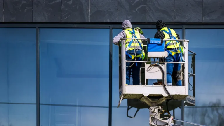 Professional window cleaners Reading using a lift to clean large glass windows of a commercial building, wearing safety gear and high-visibility jackets