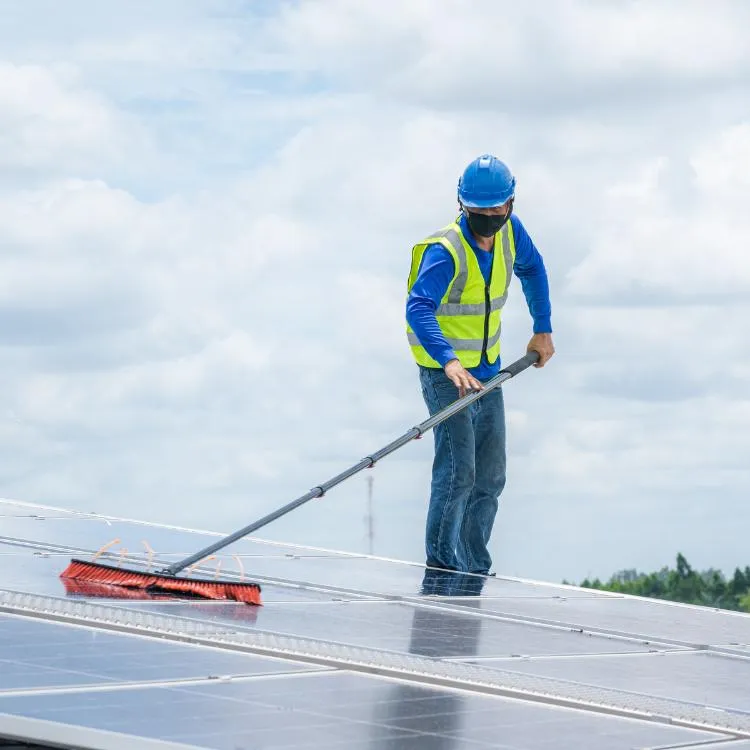 Professional worker in safety gear cleaning solar panels with a long brush. Expert solar panel cleaning services in Reading for maximum efficiency and performance